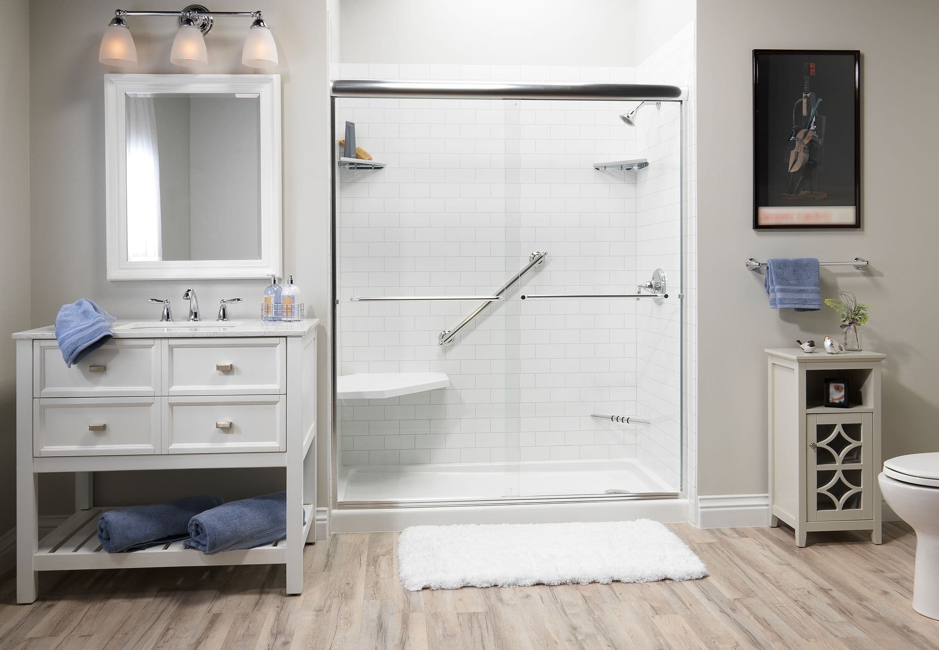 Modern bathroom with white vanity, mirror, and shower with glass doors. Wooden floor, blue towels, and a fluffy white rug create a cozy, clean feel.