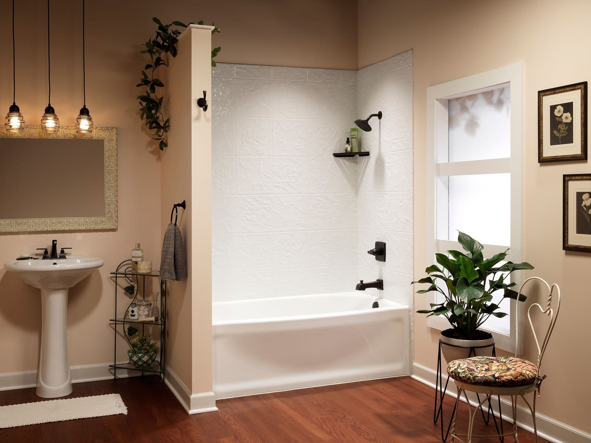 Elegant bathroom with a white tub and sink, wooden floor, and warm lighting. Greenery and framed art add a cozy, inviting feel.