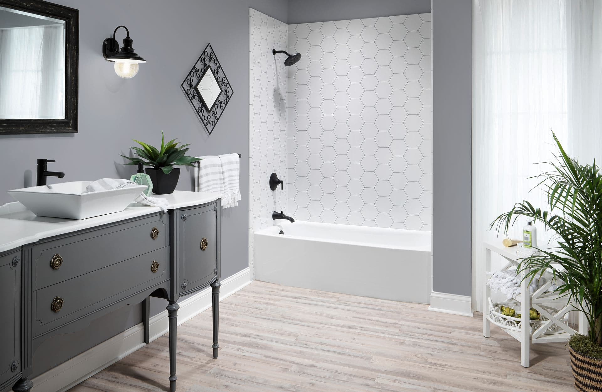 Stylish bathroom with gray walls, hexagonal tiled shower, and vintage gray vanity. Features a potted plant, light wood floors, and ample natural light.