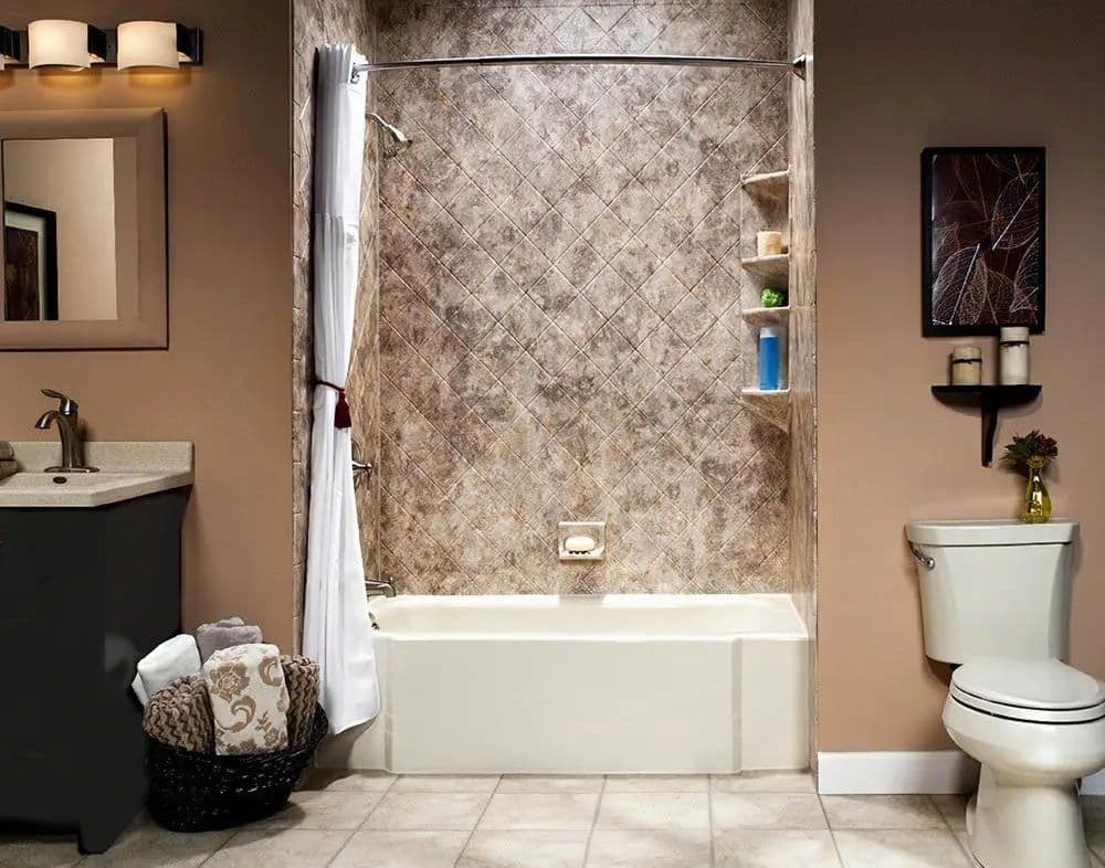 Modern bathroom with a beige tiled bathtub, white curtain, and shelves holding toiletries. A vanity with dark cabinets, mirror, and a basket of towels is on the left. A toilet with candles and a small vase is on the right, under a framed leaf print. Warm lighting creates a cozy atmosphere.