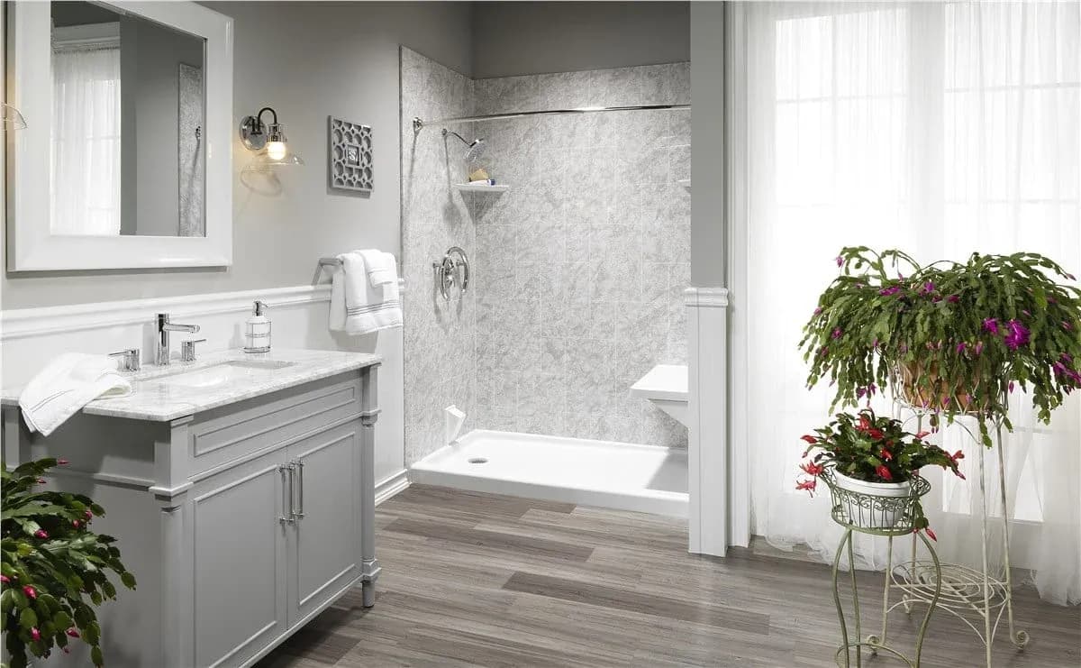 Bright bathroom with gray vanity, marble countertop, and walk-in shower. Wooden floor and lush green plants add a refreshing touch.