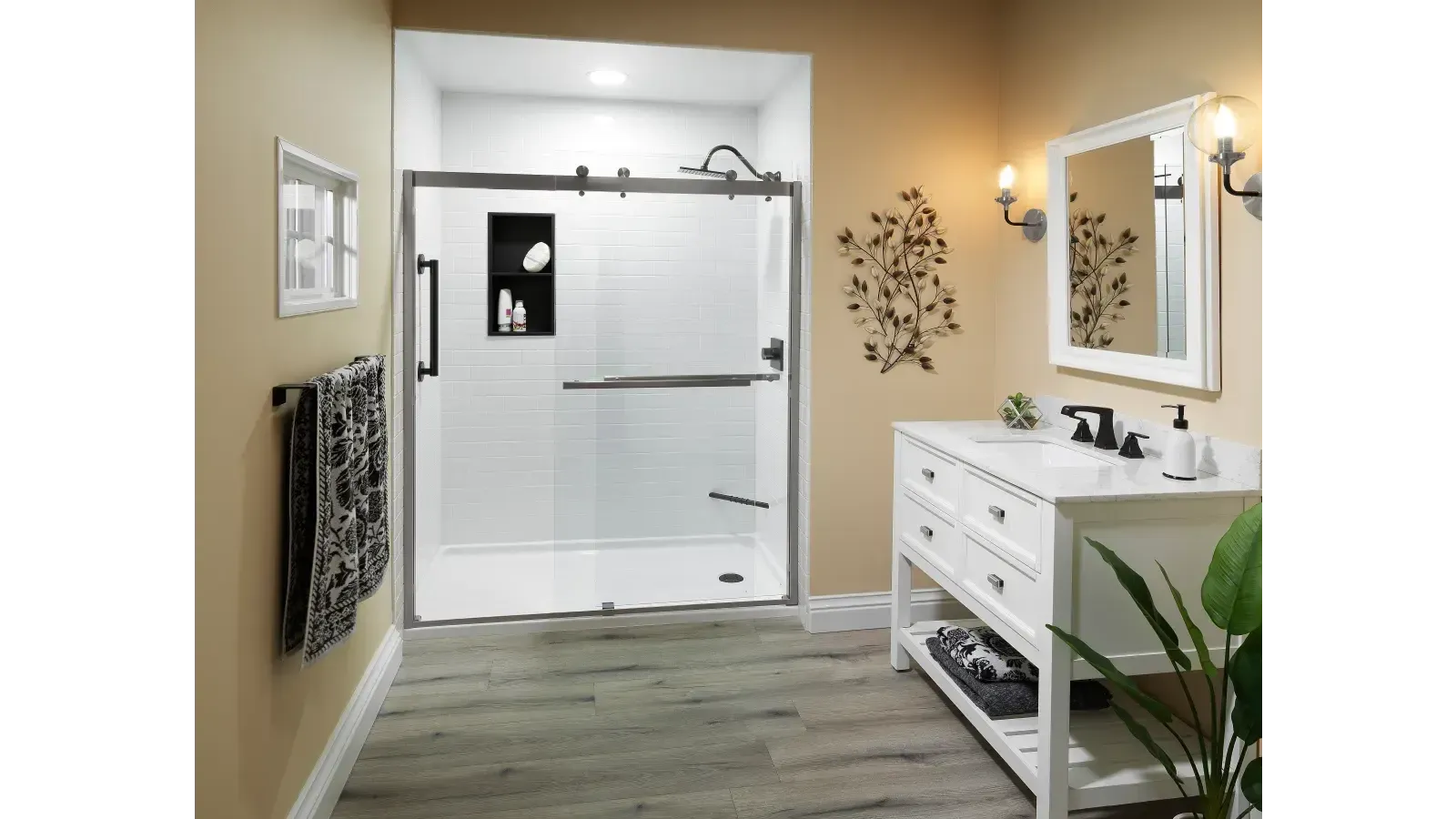 Modern bathroom with a sliding glass shower, white tiles, and shelving. Beige walls, light wood flooring, white sink cabinet, mirror, and towel rack.
