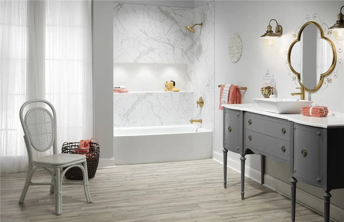 Elegant bathroom with marble accents. Features a gray vanity, oval mirror, wicker chair, and modern gold fixtures. Inviting and stylish ambiance.