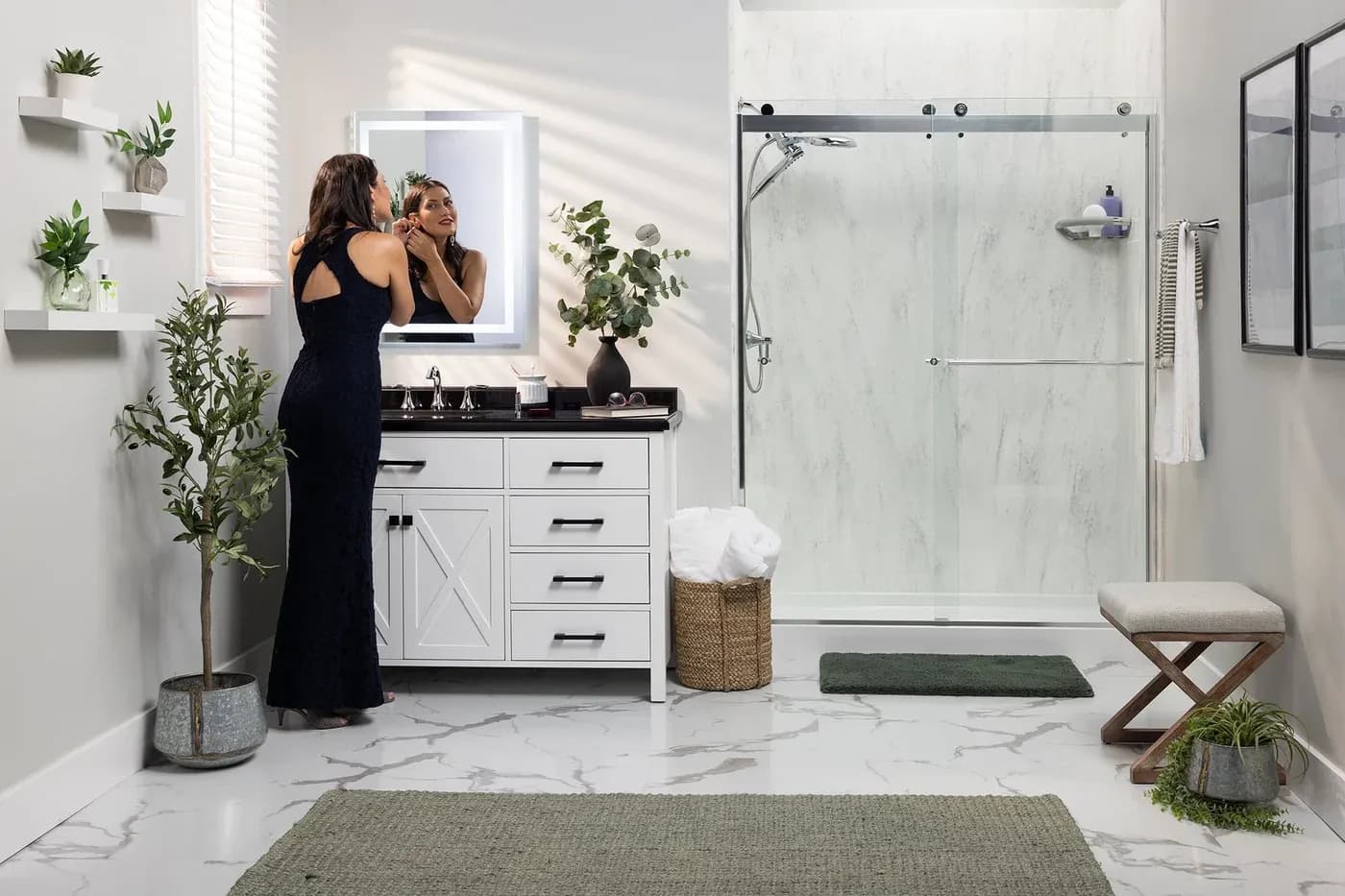 A woman in an elegant black dress applies makeup at a modern bathroom vanity with a large mirror. The room is bright with plants and a walk-in shower.