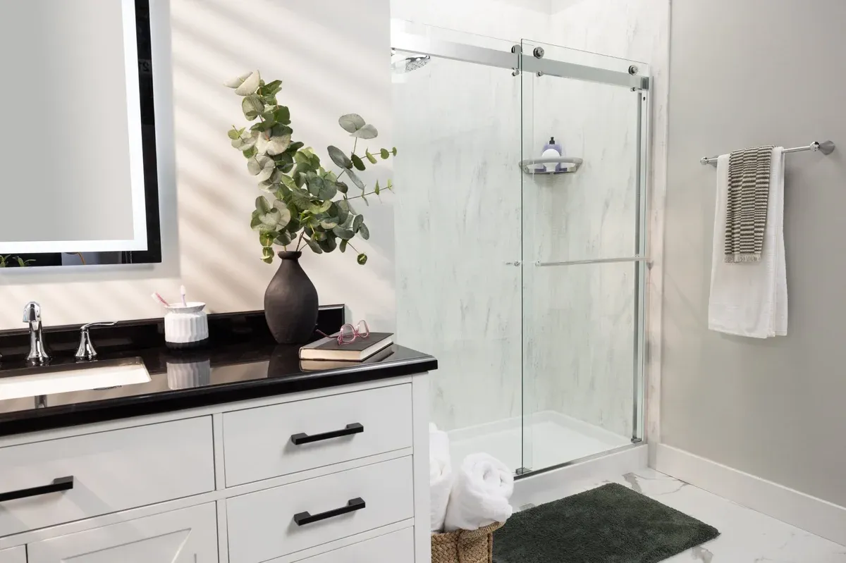 Modern bathroom with a white vanity, black countertop, and silver faucets. A glass shower is adjacent, with a towel rack and lush greenery for decor.