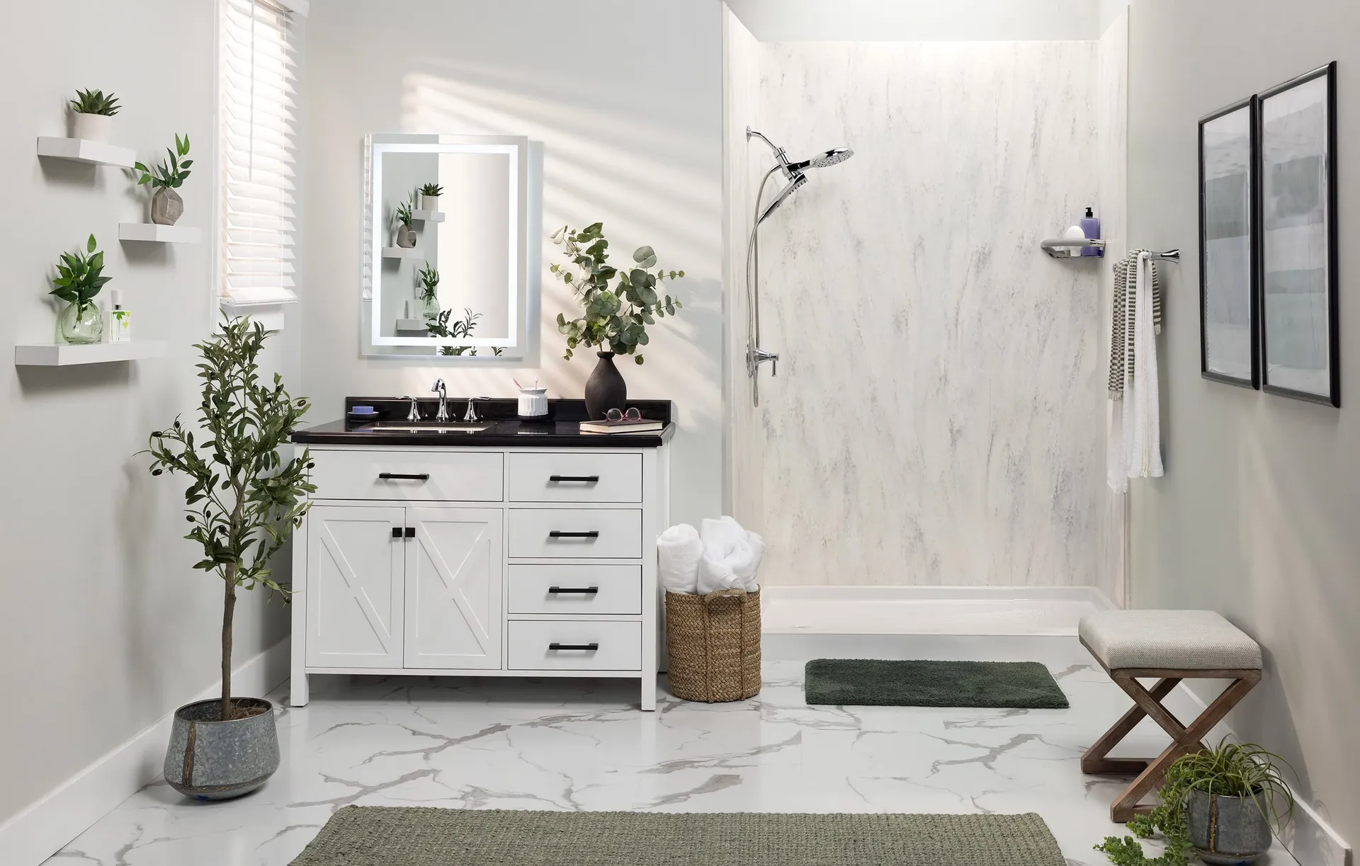 Modern bathroom with white vanity, dark countertop, and mirror. Marble shower, greenery on shelves, wicker basket, and a green rug add warmth.